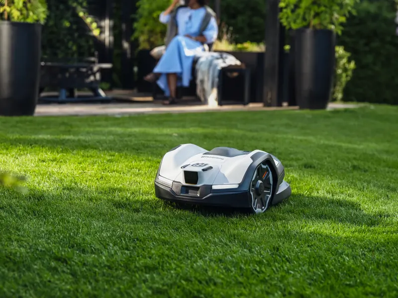 Robot tallagespa Husqvarna Automower® treballant en un jardí mentre una dona descansa a la terrassa