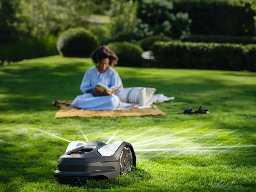 Robot tallagespa Husqvarna Automower® tallant la gespa al costat d'una noia que llegeix sobre una manta